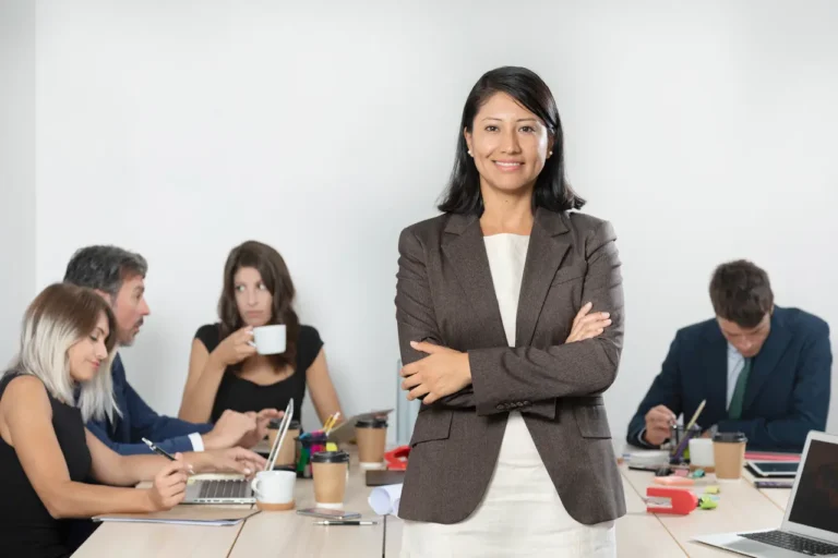 Confident businesswoman in suit standing with team working in modern office, leadership and teamwork concept.