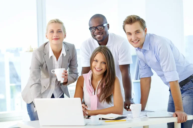 Smiling diverse business team working together at office desk with laptop, coffee, and documents